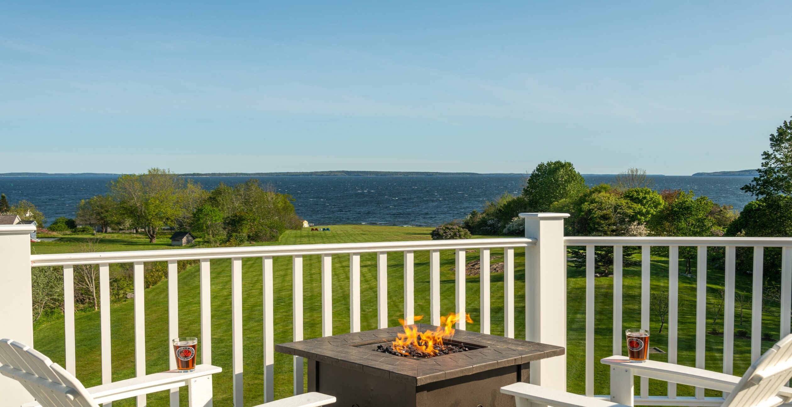 White Adirondack chairs and a firepit on the private deck overlooking the ocean 