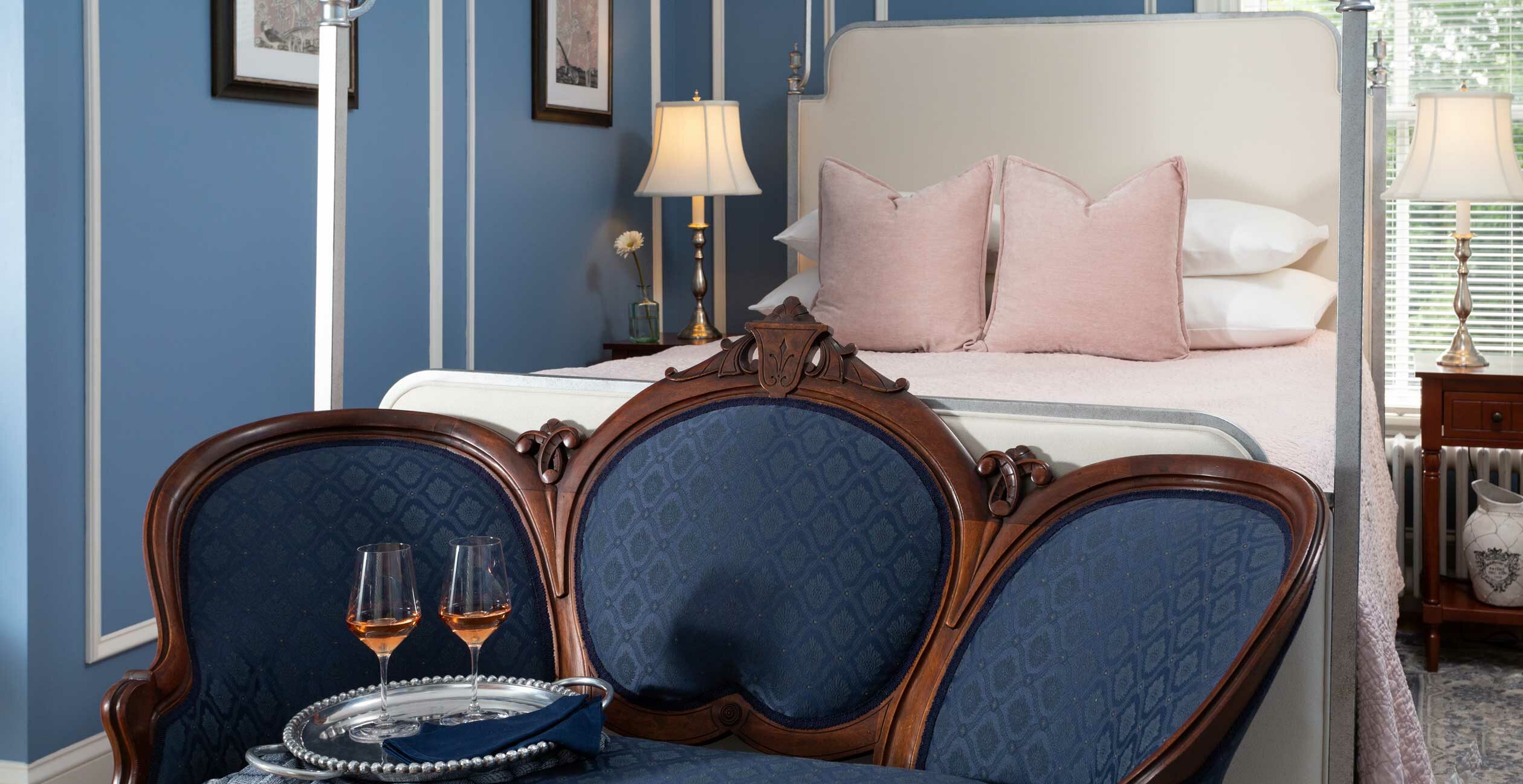 Queen bed in a room with a chair and table with two glasses of champagne