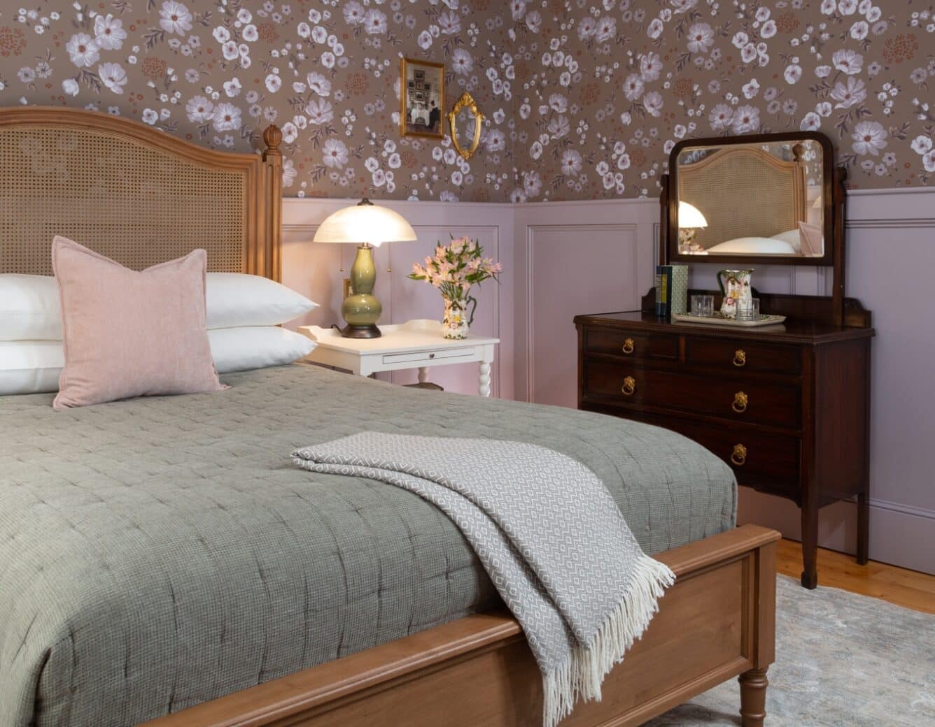 Bed in wallpapered room with antique dresser