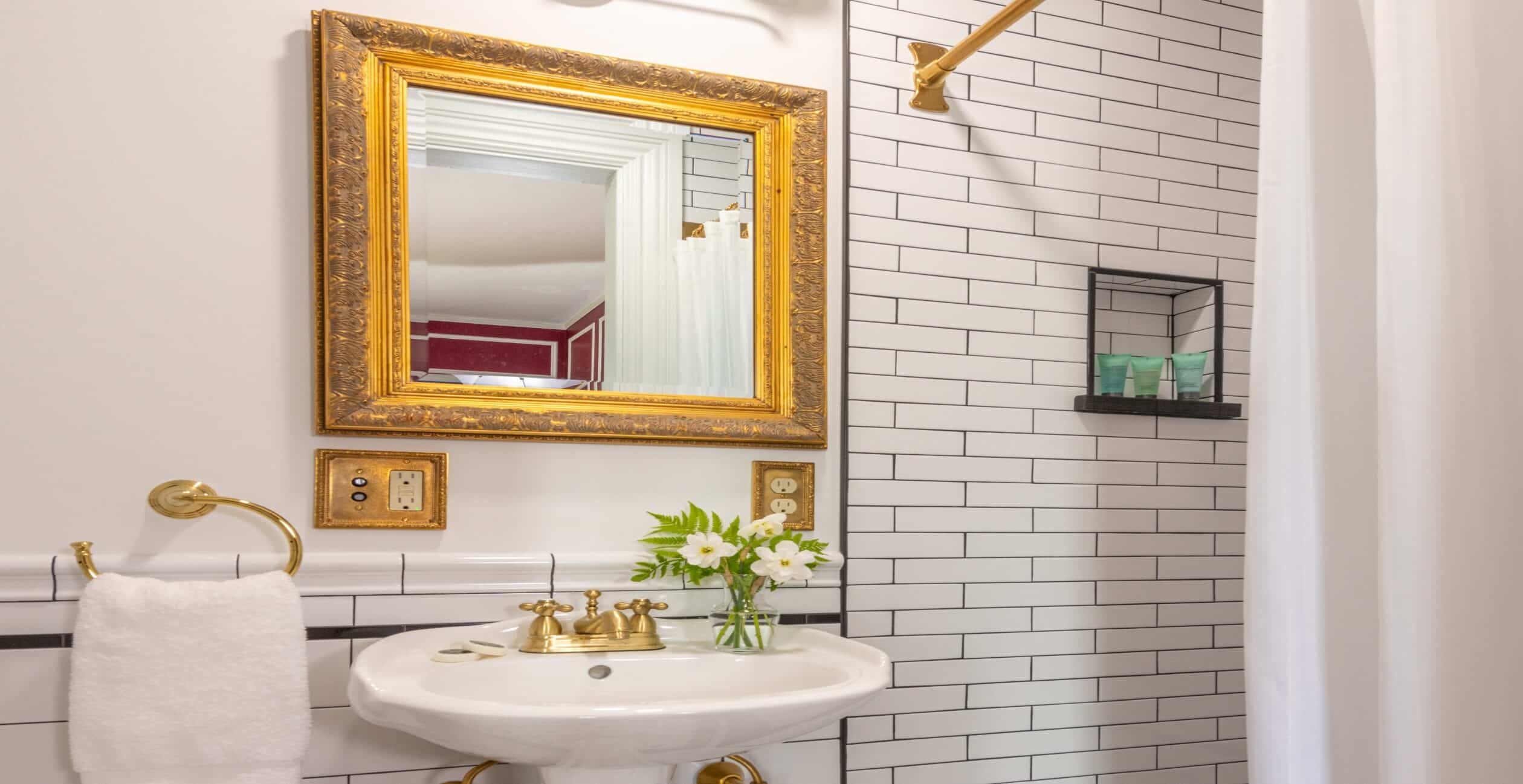 Bathroom sink and shower with white subway tiles and gold fixtures