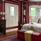 Four-poster queen bed in a room with burgundy painted walls and a fireplace