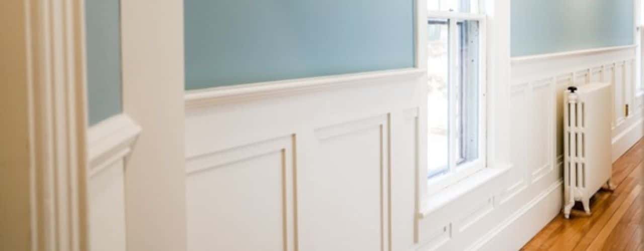 The photo shows elaborate white trim halfway up the wall, painted soft blue upper walls, and the hardwood floor. 