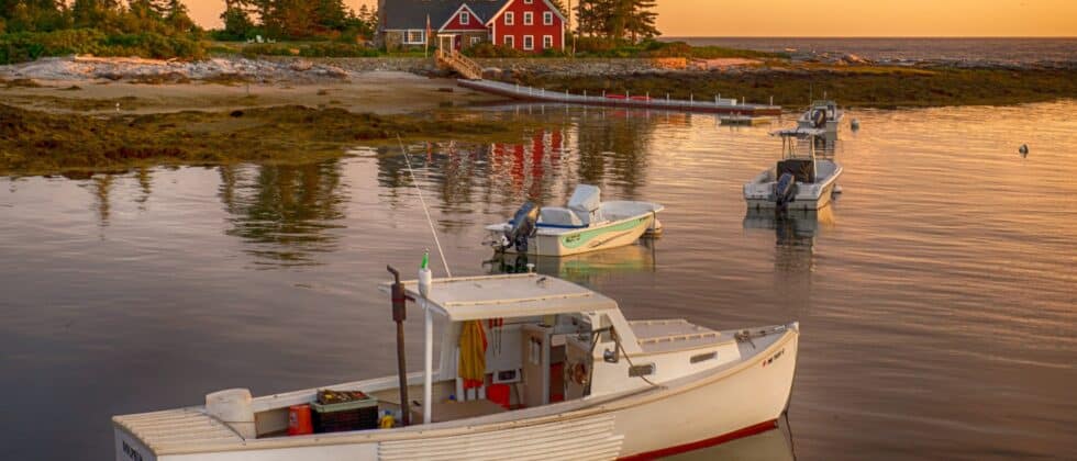Lobster boat in a cove with red house on shore